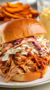 Slow cooker BBQ pulled chicken piled onto a toasted brioche bun, smothered in smoky, tangy sauce, and topped with creamy coleslaw. Served with a side of crispy sweet potato fries for a balanced, flavorful meal.